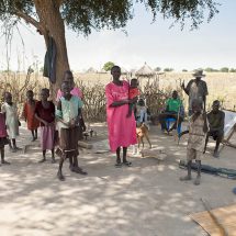 A family stands in the shade of a tree in Liliir, South Sudan @ Shutterstock/John Wollwerth