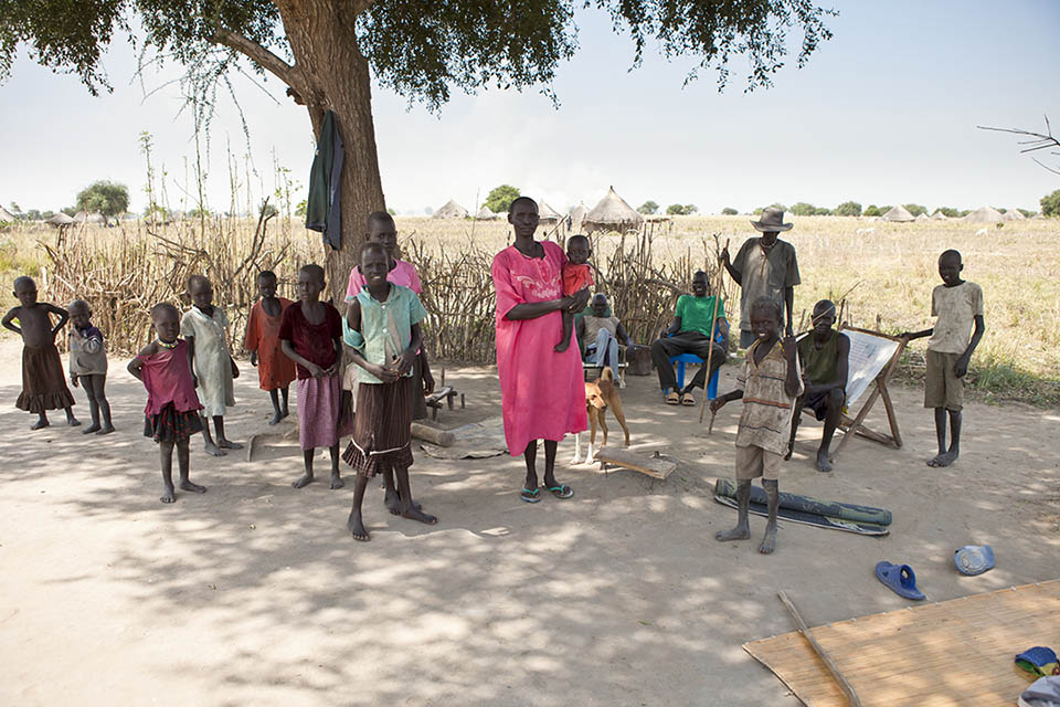 A family stands in the shade of a tree in Liliir, South Sudan @ Shutterstock/John Wollwerth